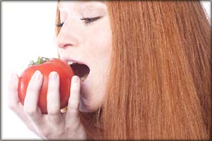 GERD diet: redheaded woman taking a bit of a tomato. Tasting a tomato.